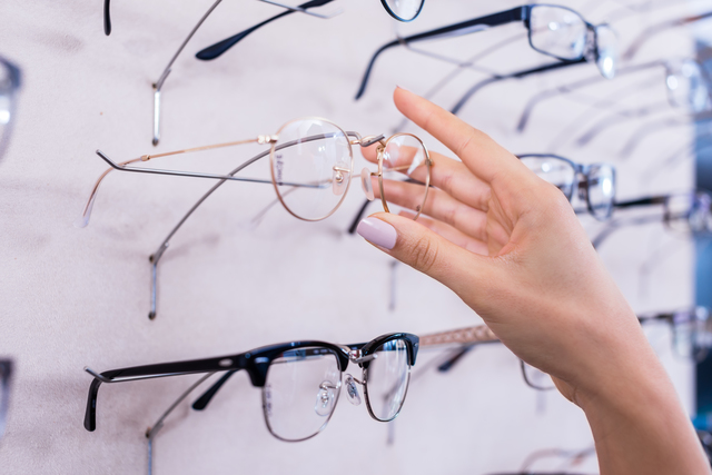 Woman taking glasses out of shelf in optician store, close up on hand